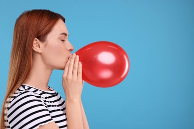 Photo of Woman inflating red balloon on light blue background, space for text