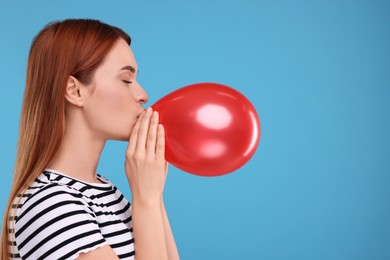 Woman inflating red balloon on light blue background, space for text