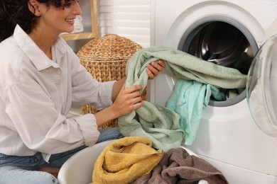 Woman taking laundry out of washing machine indoors, closeup