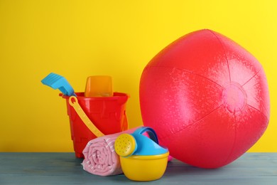 Photo of Bright beach ball, blanket and sand toys on light blue wooden table against yellow background