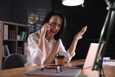 Photo of Emotional businesswoman talking on smartphone at table in office. Hate concept