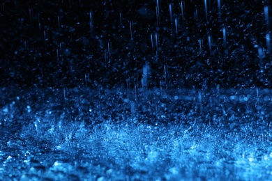 Photo of Heavy rain falling down on ground against dark background, toned in blue