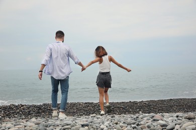 Photo of Young couple on rocky beach near sea, back view