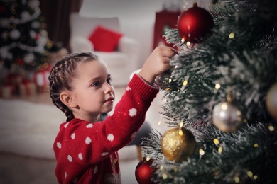 Photo of Adorable little child decorating Christmas tree at home