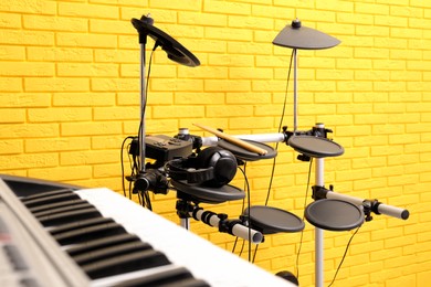 Electronic drum kit and synthesizer near yellow brick wall indoors. Musical band practice