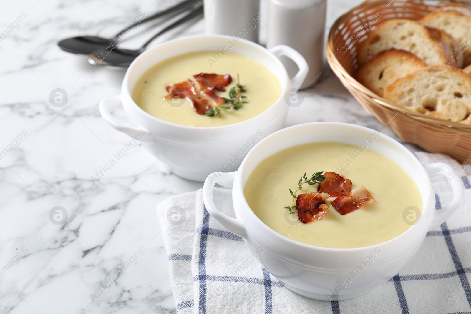 Photo of Tasty potato soup with bacon and rosemary in bowls served on white marble table