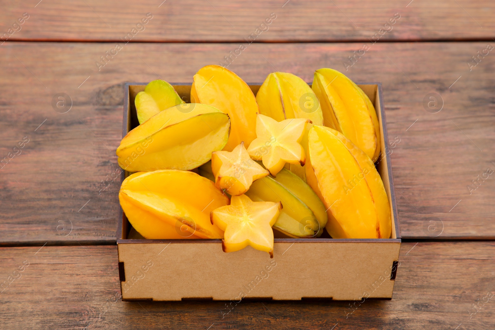 Photo of Cut and whole delicious ripe carambolas in box on wooden table