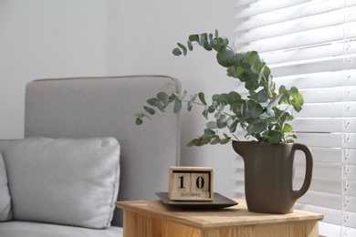 Photo of Beautiful eucalyptus branches and block calender on wooden table near window, space for text. Interior element