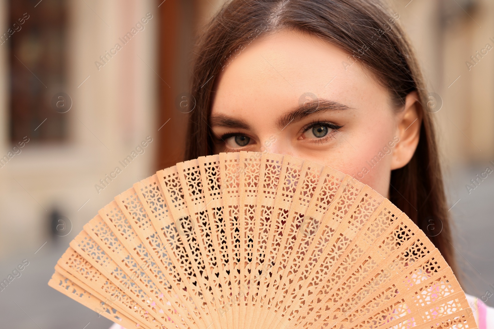 Photo of Young woman holding hand fan outdoors, closeup
