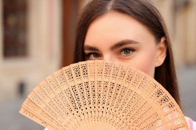 Young woman holding hand fan outdoors, closeup