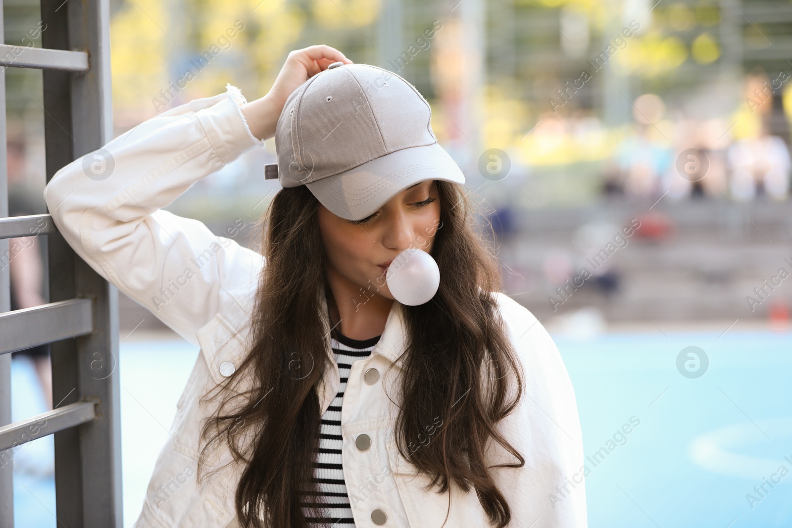 Photo of Beautiful young woman blowing bubble gum outdoors. Space for text