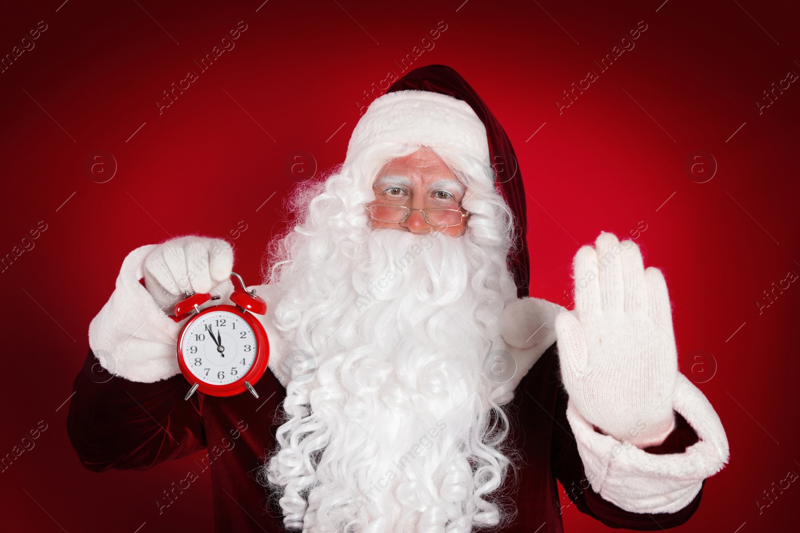 Photo of Santa Claus holding alarm clock on red background. Christmas countdown