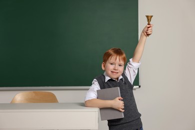 Photo of Cute little boy ringing school bell in classroom, space for text