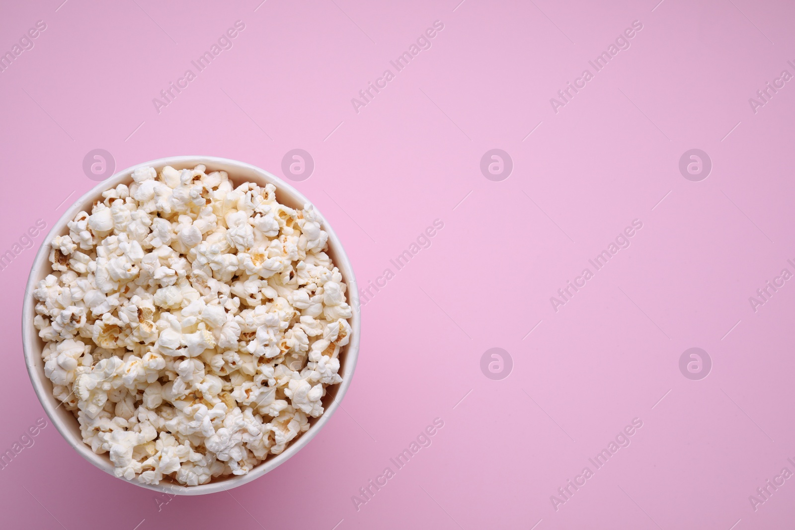 Photo of Bucket of tasty popcorn on pink background, top view. Space for text
