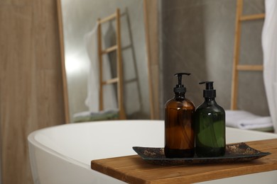 Wooden bath tray with bottles of shower gels on tub indoors, space for text