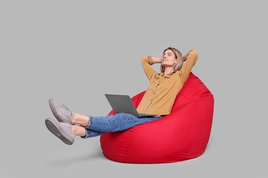 Photo of Happy woman with laptop sitting on beanbag chair against light grey background