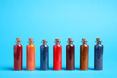 Glass bottles with different food coloring on light blue background. Space for text