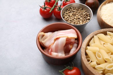 Raw pasta, bacon and fresh ingredients on light grey table, space for text