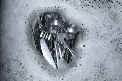 Washing silver spoons, forks and knives in foam, flat lay