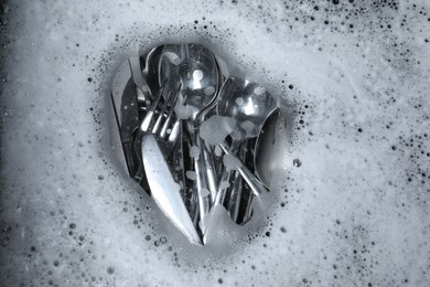 Photo of Washing silver spoons, forks and knives in foam, flat lay