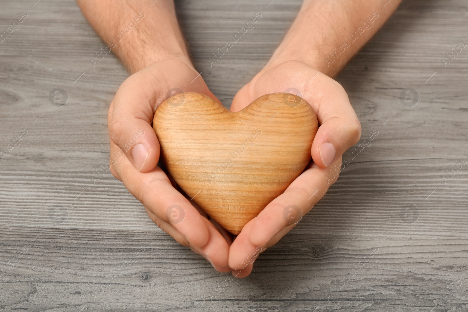 Photo of Young man holding heart on grey wooden background, closeup. Donation concept