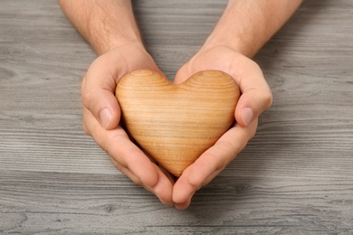 Young man holding heart on grey wooden background, closeup. Donation concept