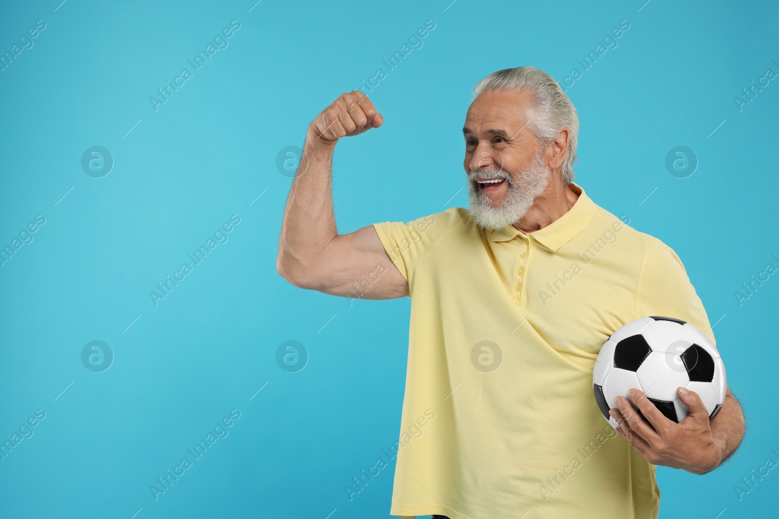 Photo of Happy senior sports fan with soccer ball on light blue background, space for text