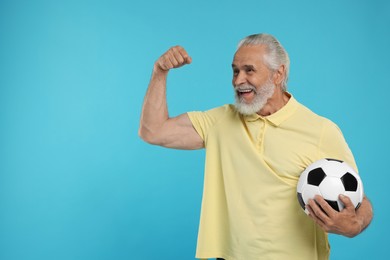 Happy senior sports fan with soccer ball on light blue background, space for text