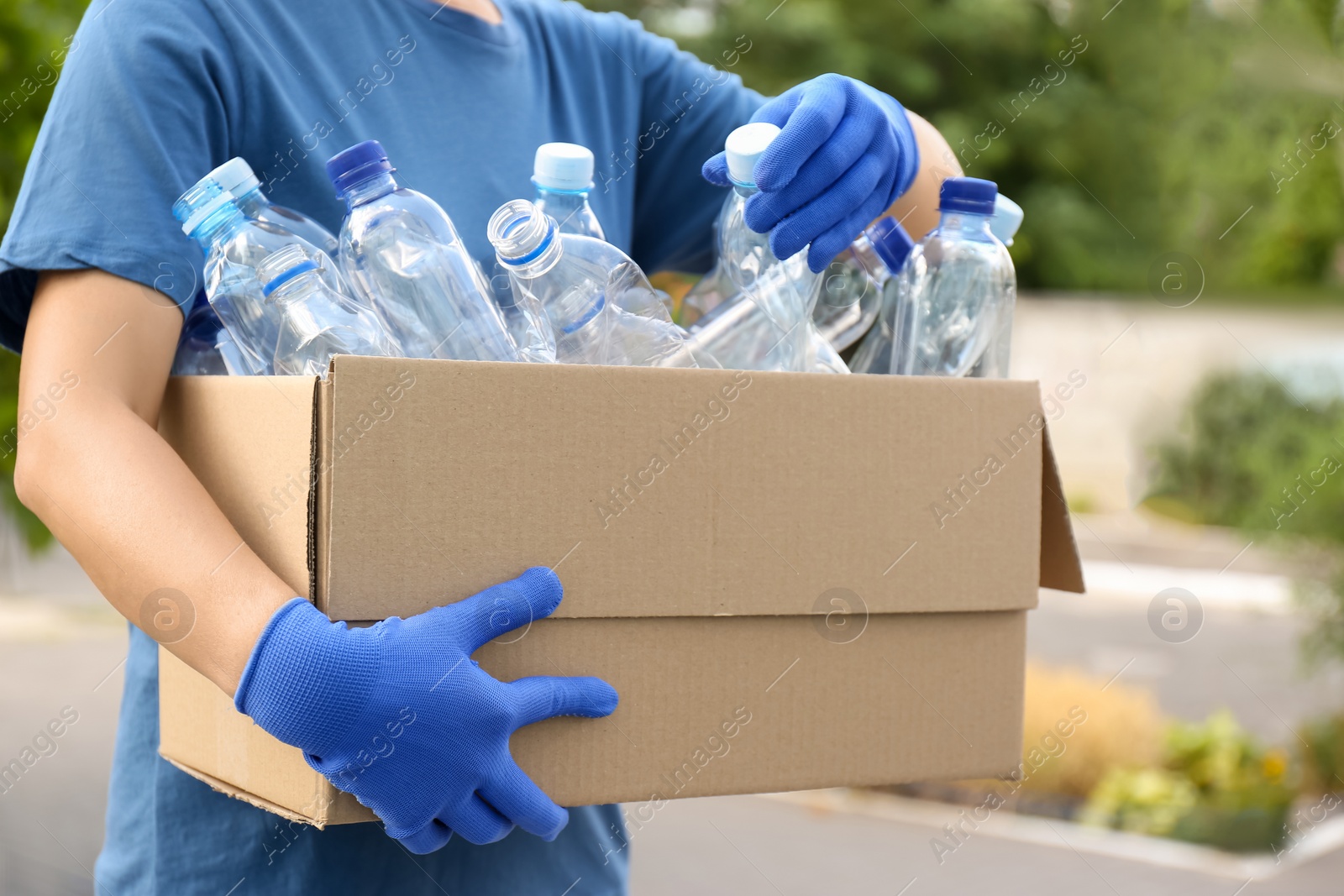 Photo of Woman holding cardboard box with used plastic bottles outdoors, closeup. Recycling problem