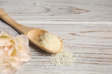 Photo of Spoon with yellow sea salt and flower on white wooden table, closeup. Space for text