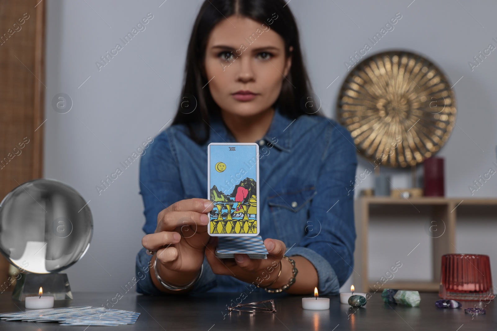 Photo of Fortune teller with tarot card Eight of Cups at grey table indoors, focus on hands