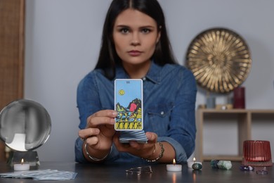 Photo of Fortune teller with tarot card Eight of Cups at grey table indoors, focus on hands