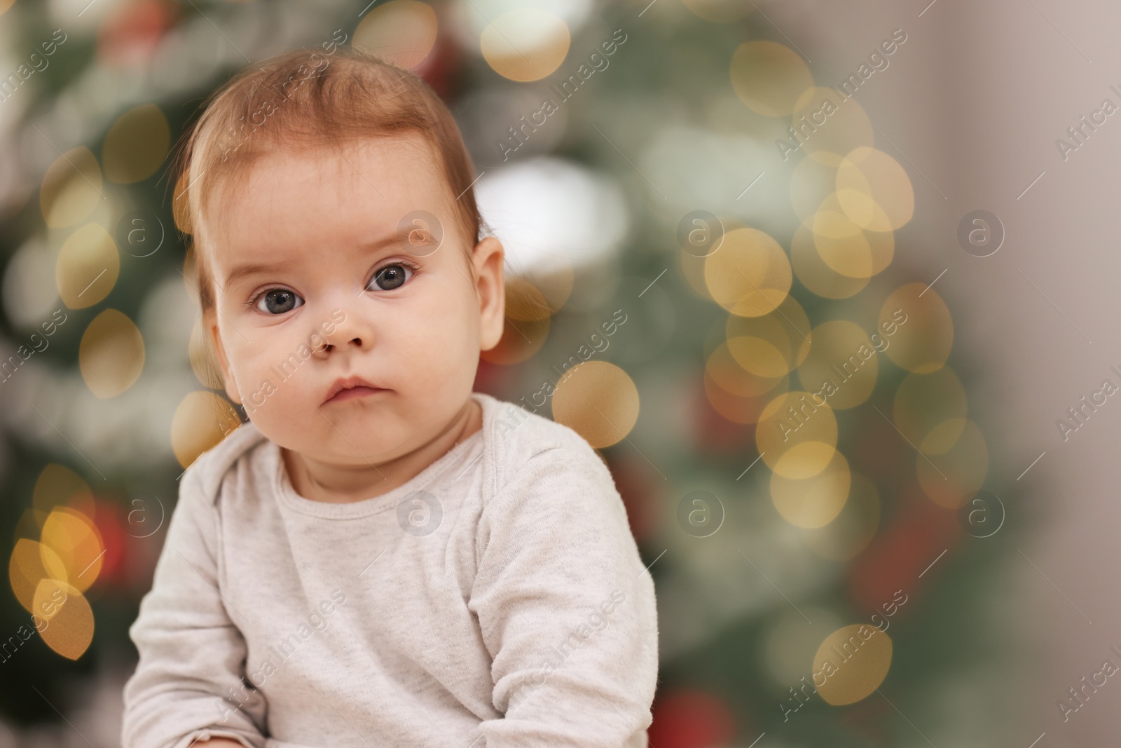 Photo of Cute little baby against blurred festive lights, space for text. Winter holiday