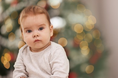 Photo of Cute little baby against blurred festive lights, space for text. Winter holiday