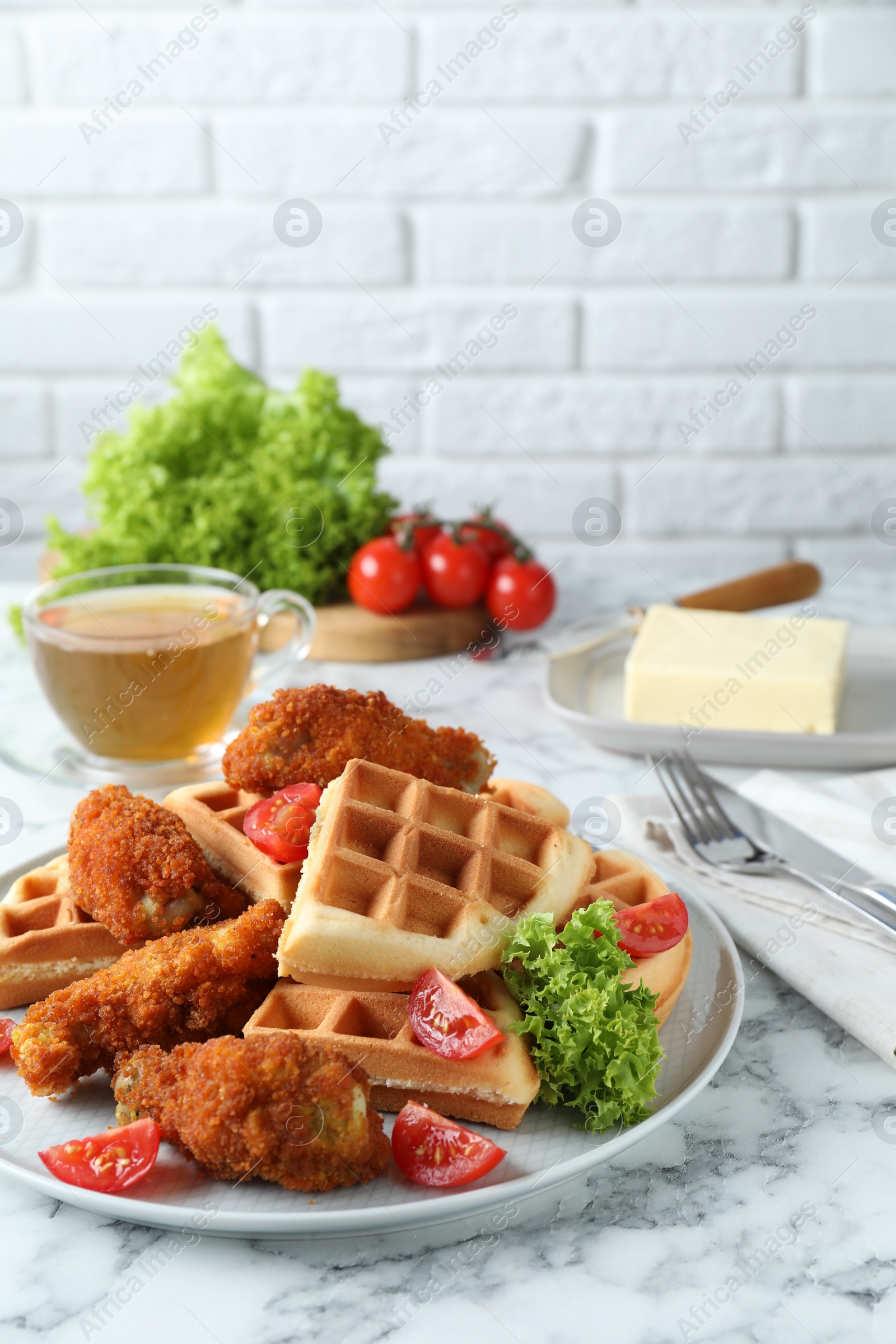 Photo of Tasty Belgian waffles served with fried chicken, tomatoes and lettuce on white marble table