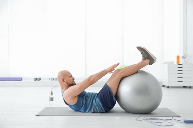 Photo of Overweight man doing exercise with fitness ball in gym