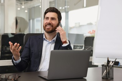 Man with laptop talking on phone at black desk in office