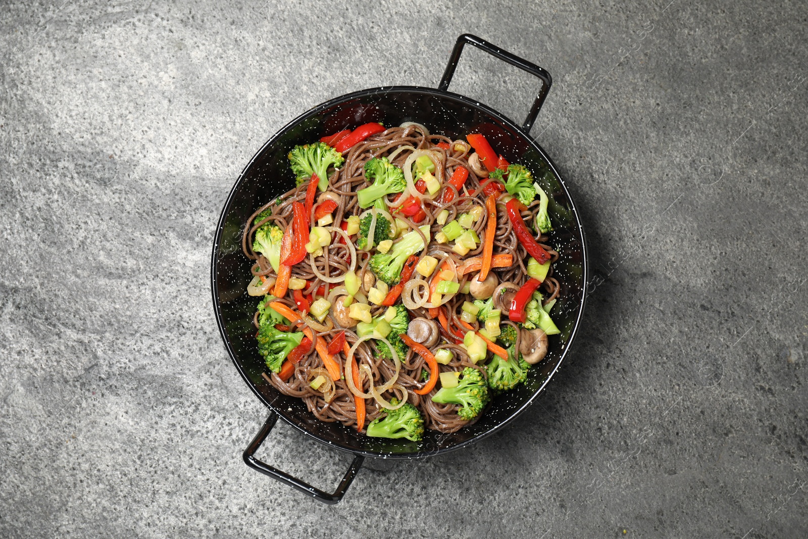 Photo of Stir fried noodles with mushrooms and vegetables in wok on grey table, top view