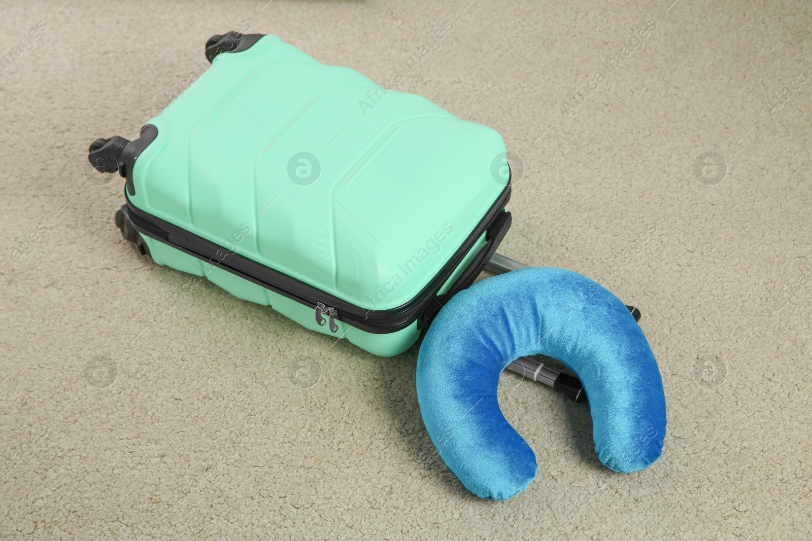 Photo of Light blue travel pillow and suitcase on beige rug