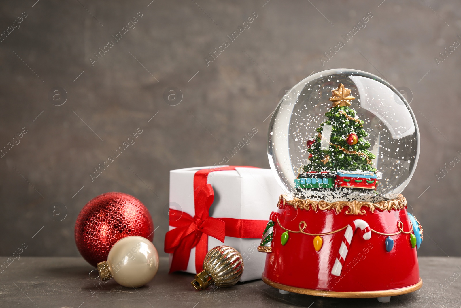 Photo of Beautiful snow globe, gift box and Christmas balls on grey table