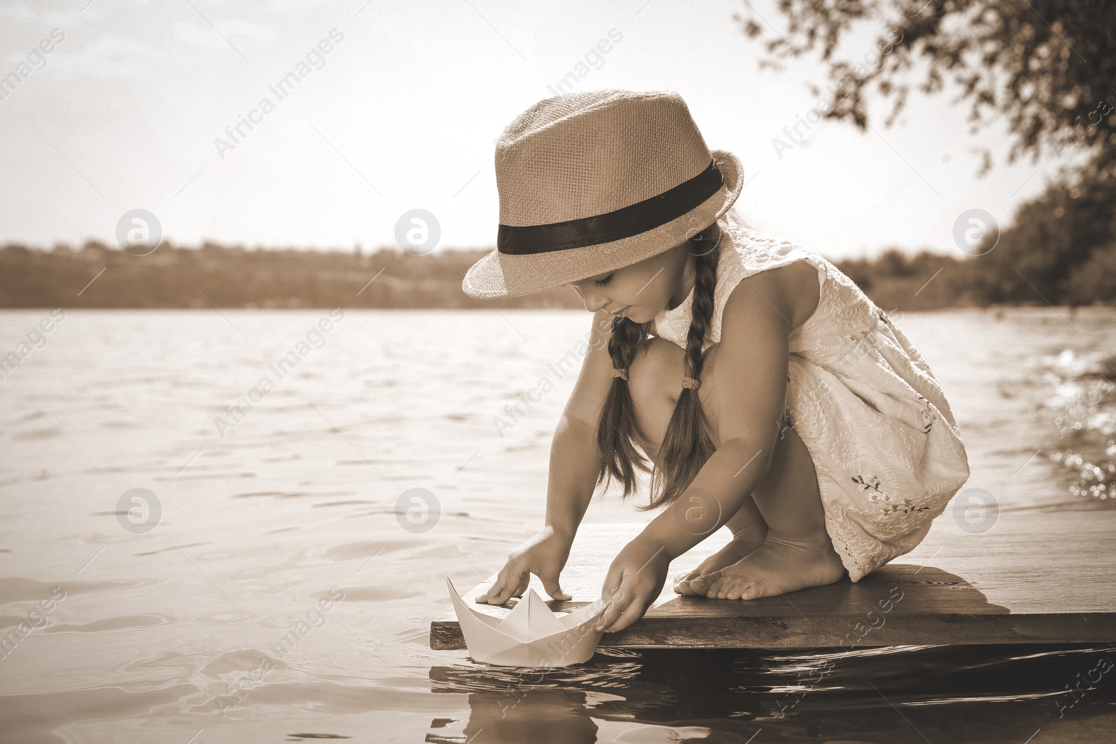 Image of Cute little girl playing with paper boat on wooden pier near river. Retro photo effect