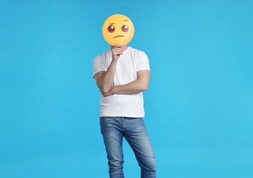 Photo of Man covering face with thinking emoticon on light blue background