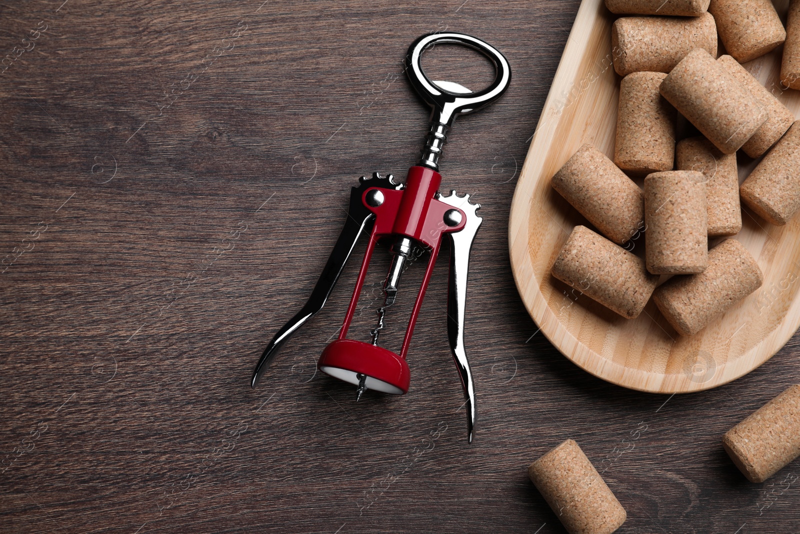 Photo of Corkscrew and wine bottle stoppers with plate on wooden table, flat lay