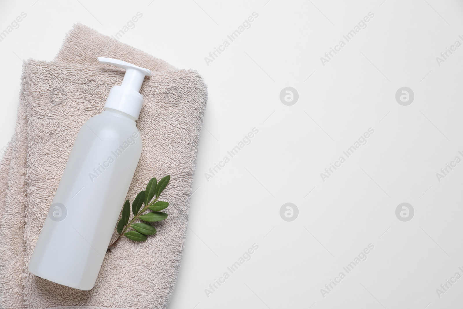 Photo of Bottle of cosmetic product, green leaves and soft towel on white background, top view. Space for text