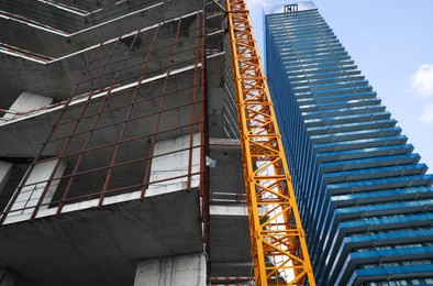 Photo of Construction site with tower crane near buildings, low angle view