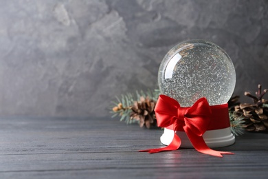 Beautiful Christmas snow globe with red bow on grey wooden table, space for text