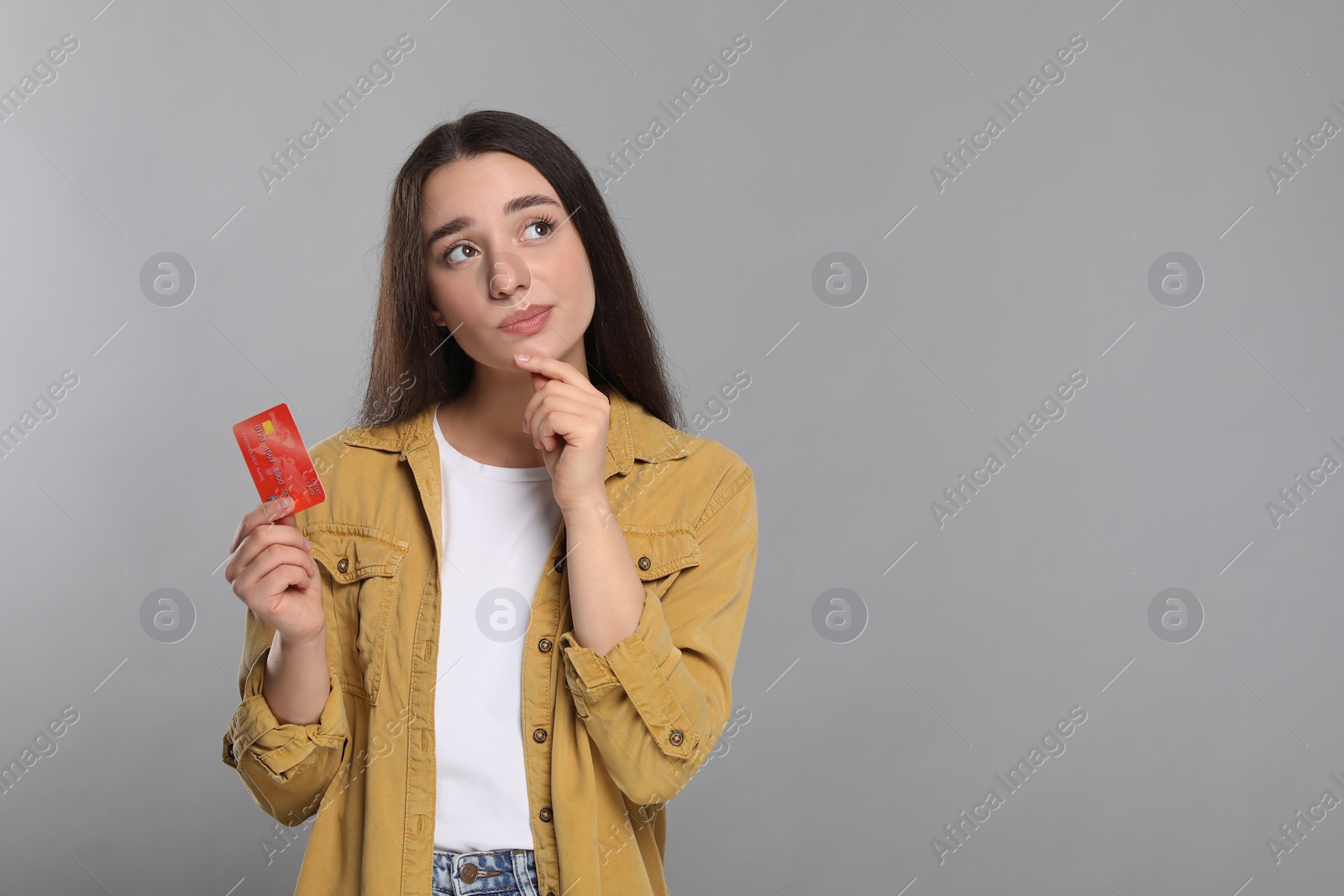 Photo of Curious woman with credit card on light gray background, space for text. Debt limit
