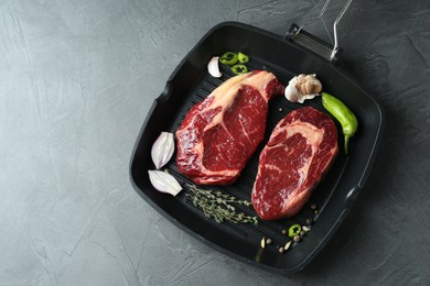 Photo of Grill pan with pieces of fresh beef meat, thyme and spices on gray table, top view. Space for text