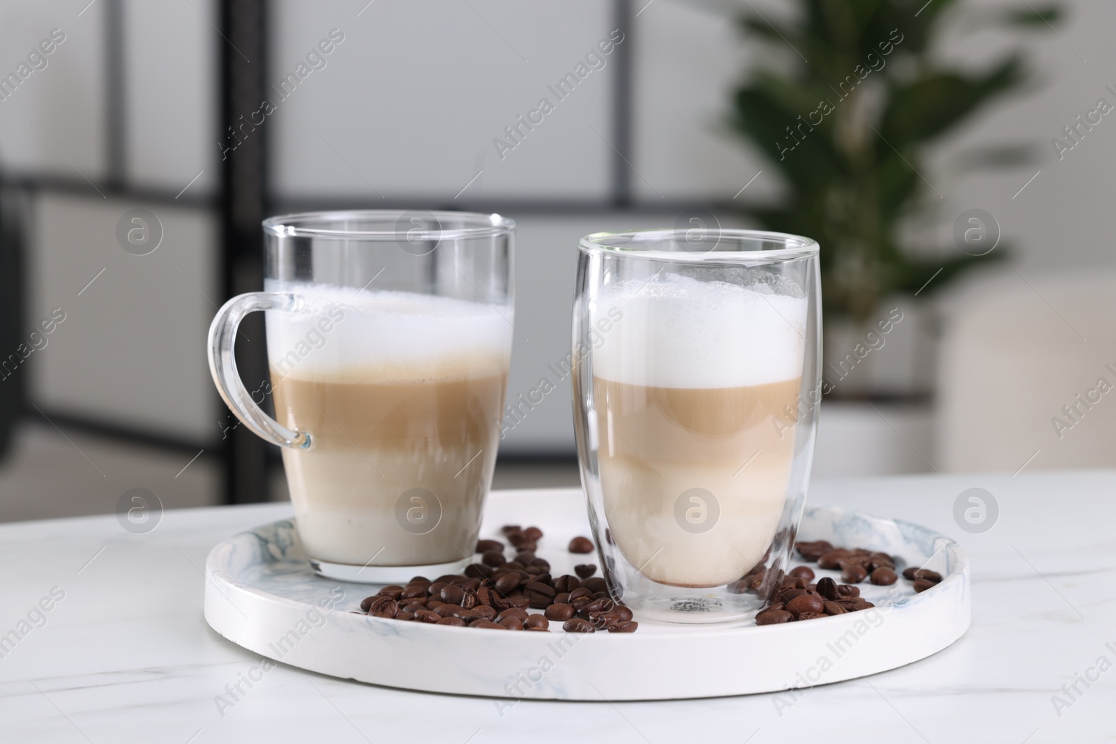 Photo of Aromatic latte macchiato and coffee beans on white marble table against blurred background