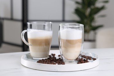 Photo of Aromatic latte macchiato and coffee beans on white marble table against blurred background